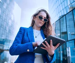 Woman in a blue blazer reading from a tablet by a window